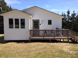 a small white house with a wooden deck at Bubbling Brook Cottages in Cavendish