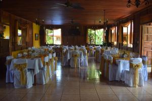 Una habitación llena de mesas con arreglos de mesa blancos y amarillos. en Hotel y Restaurante Las Tablitas, en Alajuela