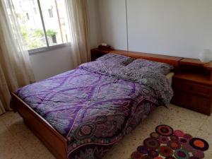 a bedroom with a bed with a purple comforter and a window at Family Nest In The Heart Of Limassol in Limassol