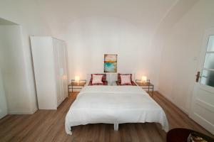 een witte slaapkamer met een groot wit bed met rode kussens bij Galéria Apartman in Veszprém