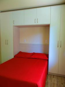 a bedroom with a red bed and white cabinets at Residencial Recanto Paraíso BC - Flat in Balneário Camboriú