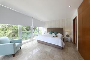 a bedroom with a bed and a chair and windows at Terrazas Apartments by Bahia Principe in Tulum