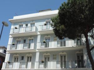 a white building with balconies and a tree at Hotel Liliana in Rimini