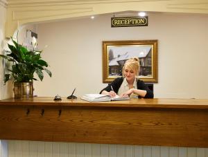 a woman sitting at a reception desk with a book at Roebuck by Greene King Inns in Forest Row