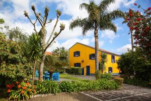 Quinta das Flores في كابيلاس: منزل أصفر مع أشجار النخيل والنباتات