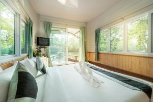 a bedroom with a large white bed with windows at รตะธารา รีสอร์ท ratathara resort in Ban Khlong Tamru