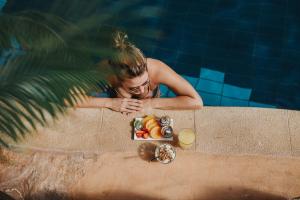 a woman standing next to a pool with a tray of food at Cnaan Village Boutique Hotel & Spa in Had Nes