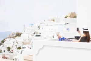 Una donna seduta su un cornicione che scatta una foto di una città di Agave Santorini Design Boutique Hotel a Imerovigli