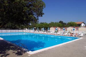 a large blue swimming pool with chairs and trees at Adriatico Family Camping Village in Cervia
