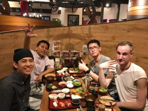 宮崎市にあるゲストハウス宮崎 guesthouse miyazaki バックパッカー向け個室旅人宿 P有宮崎駅1km喫煙者不可の食卓に座って食べ物を食べる男たち