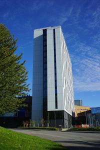 um edifício de vidro alto com uma árvore em frente em Pingvinhotellet UNN Tromsø em Tromsø