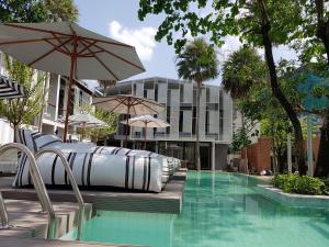 a swimming pool with chairs and umbrellas next to a building at Treevana Club Chiangmai in Chiang Mai