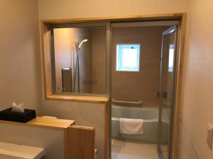 La salle de bains est pourvue d'une douche, d'une baignoire et d'un miroir. dans l'établissement Tsuru Apartments, à Furano