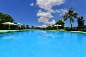 una gran piscina azul con 2 sombrillas blancas en Coco Garden Resort Okinawa, en Uruma