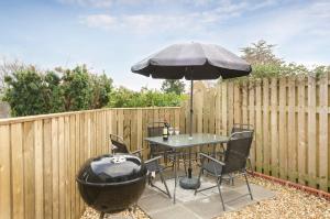 a patio with a table with an umbrella and a grill at 33 The Fairway in Newton Ferrers