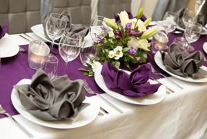 une table avec des plaques blanches, des serviettes et des fleurs violettes dans l'établissement Hotel Am Markt, à Oebisfelde