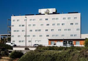 un grand bâtiment blanc avec des voitures garées dans un parking dans l'établissement B&B HOTEL Valencia Aeropuerto, à Paterna