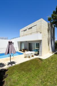 a modern house with a swimming pool and an umbrella at Pé na Areia - Guest House in Vila Real de Santo António
