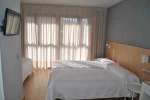 a bedroom with a white bed and a large window at Hostal Universitat in Cervera