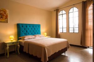 a bedroom with a bed with a blue headboard and two windows at Posada Las Flores in Guatemala