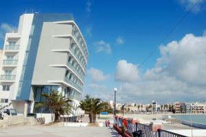 a tall white building next to a beach at Water's Edge Hotel in Birżebbuġa