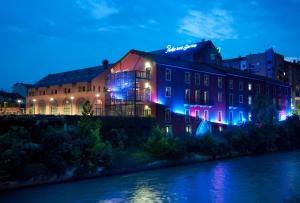 トリノにあるパシフィック ホテル フォルティノの川の隣の青紫の灯りを持つ建物
