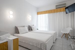 a white bedroom with two beds and a television at Alkistis Beach Hotel - Adults Only in Agios Stefanos +37 photos
