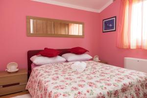 ブロダリツァにあるApartmani Nadaのピンクの壁のベッドルーム1室、赤い枕付きのベッド1台が備わります。