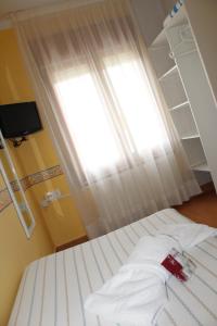 1 cama con sábanas blancas en una habitación con ventana en Hostal Fabrellas, en Caldes de Malavella