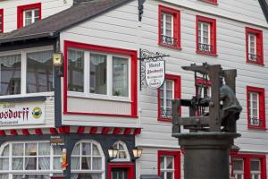 ein weißes Gebäude mit roten Fenstern und einer Statue davor in der Unterkunft Hotel Flosdorff - Appartements in Monschau