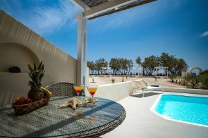 a table with two glasses of wine on a patio with a swimming pool at Sea Sound White Katikies in Perivolos