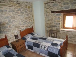 1 dormitorio con 2 camas y pared de piedra en Hotel rural Valtarranz, en Noceco
