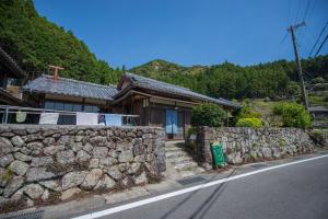 a house with a stone wall next to a road at Homestay at Remote Organic Farm in Nachikatsuura