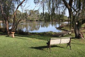 a park bench sitting in the grass near a lake at Little Lake Cottage in Nyora