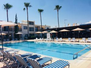 a swimming pool with chairs and umbrellas and palm trees at Carina Hotel Apartments in Ayia Napa