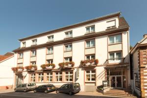 un grand bâtiment blanc avec des voitures garées devant lui dans l'établissement Hotel Majestic Alsace - Strasbourg Nord, à Niederbronn-les-Bains