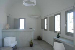 Habitación blanca con sillas blancas, mesa y ventanas en Aplai Dome, en Oia