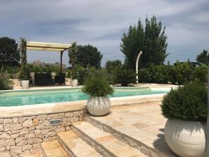 una piscina con 2 grandes jarrones blancos con plantas en Cappelluzzo, en Cisternino