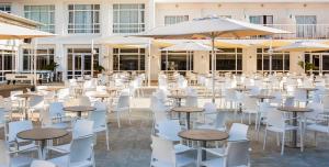 an outdoor patio with tables and white chairs and umbrellas at Globales Condes de Alcudia in Port d'Alcudia