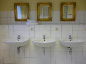 three sinks in a bathroom with three mirrors at Hostel & Bistro Haus der Horizonte in Bad Doberan