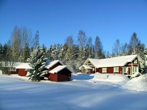 une maison recouverte de neige avec un arbre dans la cour dans l'établissement Männikkölän Pirtti, à Nurmes