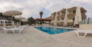 a resort with a pool with white chairs and umbrellas at Golden days in Afantou