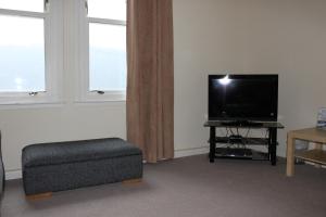 a living room with a flat screen tv and a ottoman at Carrick Farm Lochside Appartment (GF) in Lochgoilhead