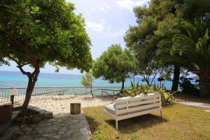 a white bench sitting on the grass near the ocean at Maison La Mer in Agia Paraskevi