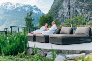 a man and woman sitting on a couch with mountains in the background at Hotel Union Geiranger Bad & Spa in Geiranger