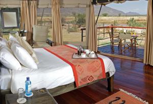 a bedroom with a bed and a balcony with a table at Ashnil Samburu Camp in Archers Post