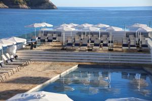 a swimming pool with chairs and umbrellas and the ocean at Mar Azul Pur Estil Hotel & Spa in Cala Ratjada