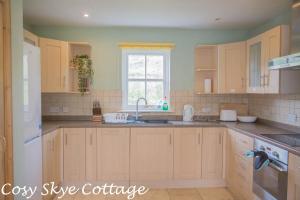a kitchen with wooden cabinets and a sink and a window at Cosy Skye Cottage in Kingsburgh