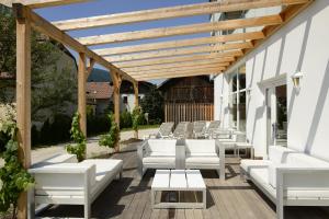 a patio with white chairs and a wooden pergola at Hotel Gassenwirt in Chienes