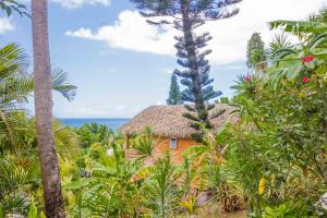 a house with a thatched roof in the middle of trees at Carre Royal in Deshaies